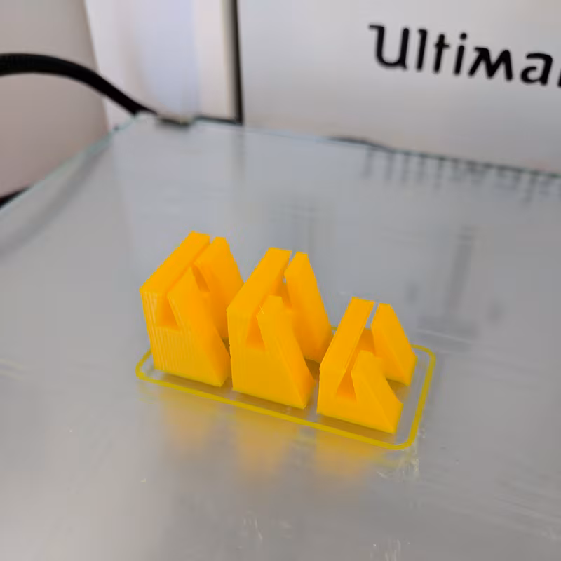 Three yellow printed holders finished on the printer bed, each showing the wedge-shaped slot
