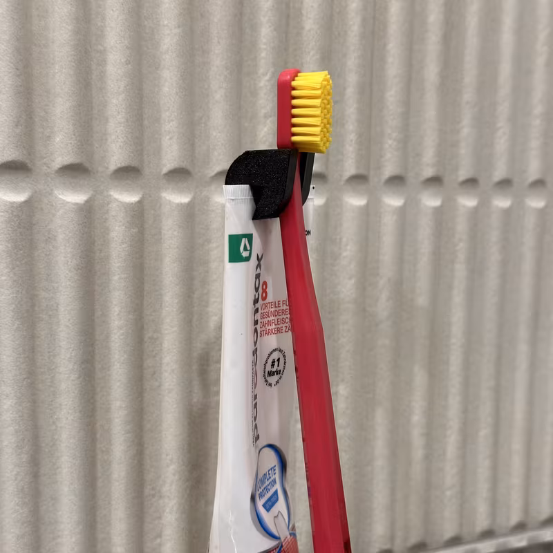 The final black holder in a bathroom, holding a pink toothbrush upright on a tube standing on its cap