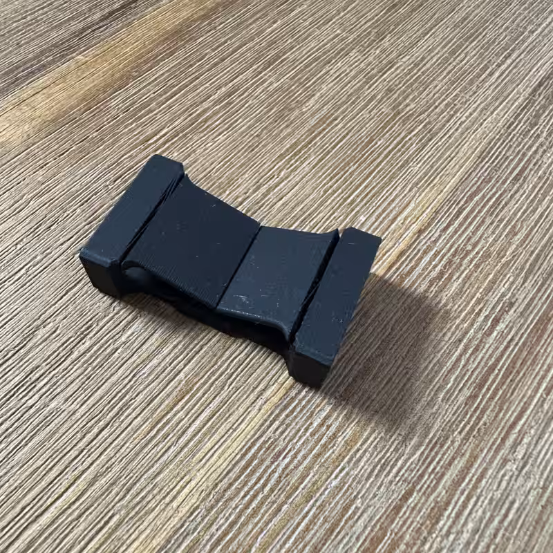 The black printed part seen at an angle, showing the waisted bar shape with a flanged slot at each end