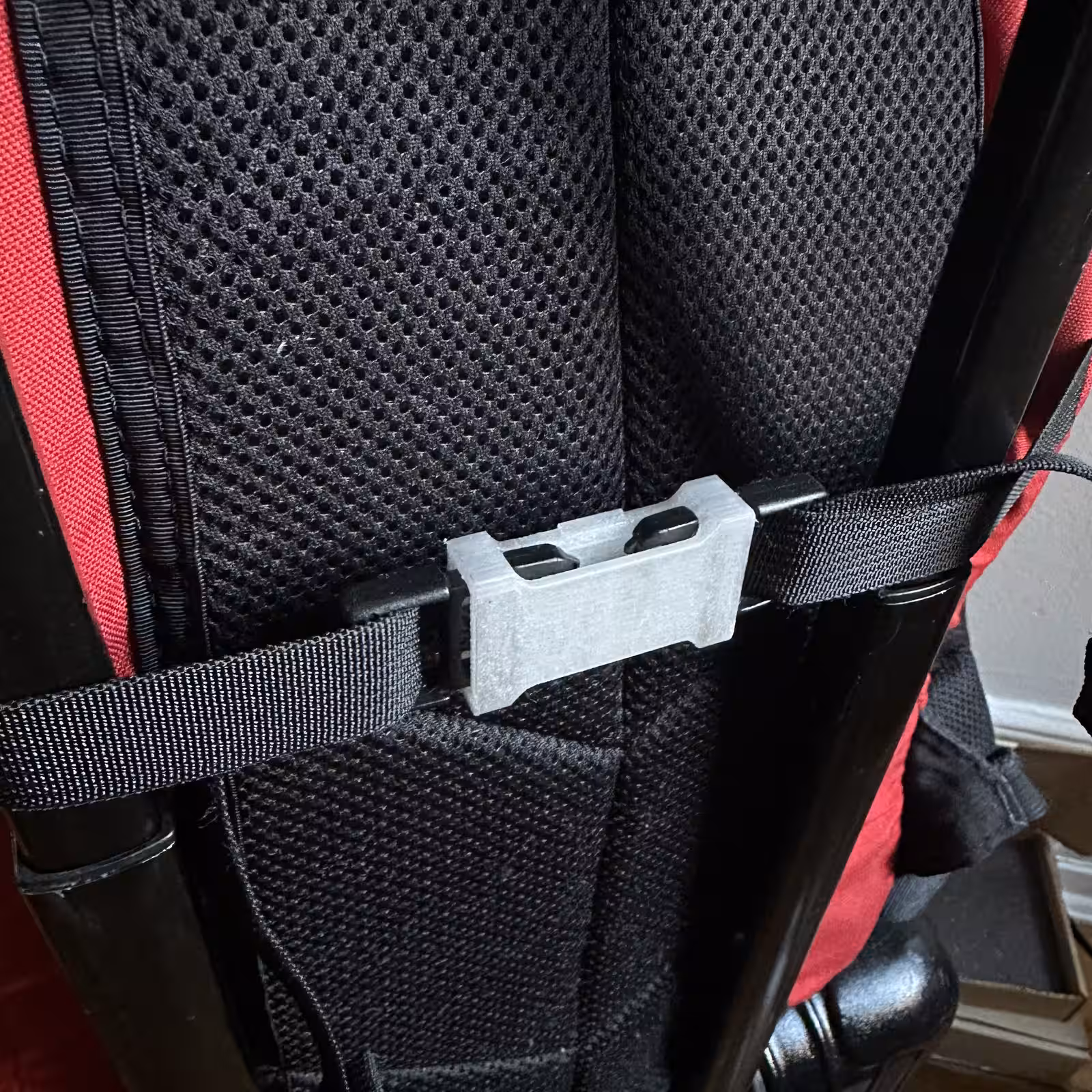 Close-up of the white printed part joining two black webbing straps across the padded shoulder harness of a red backpack