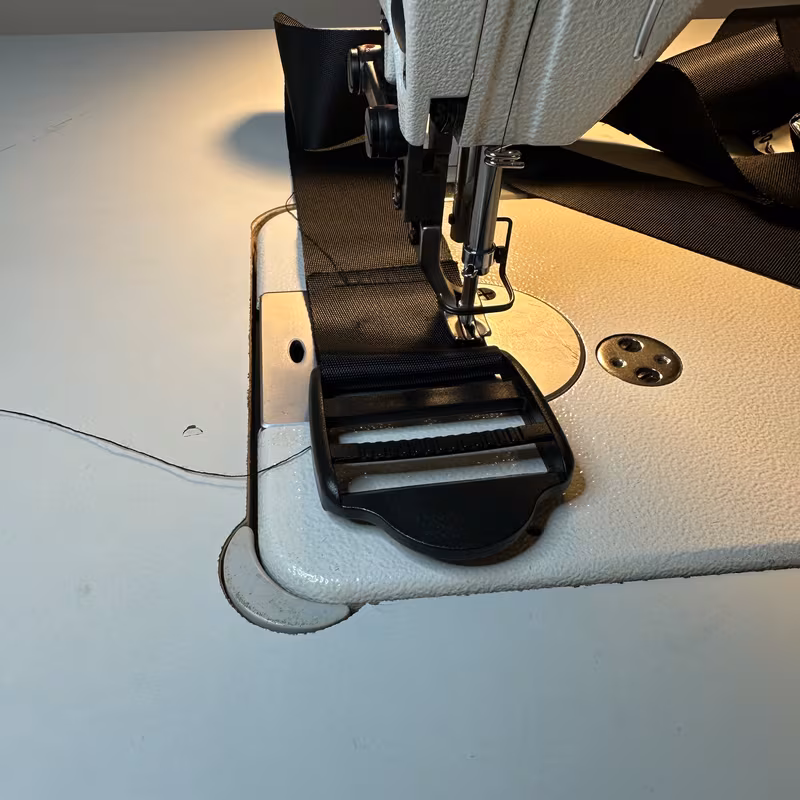 Close-up of the machine sewing a black side-release buckle onto the end of a length of webbing