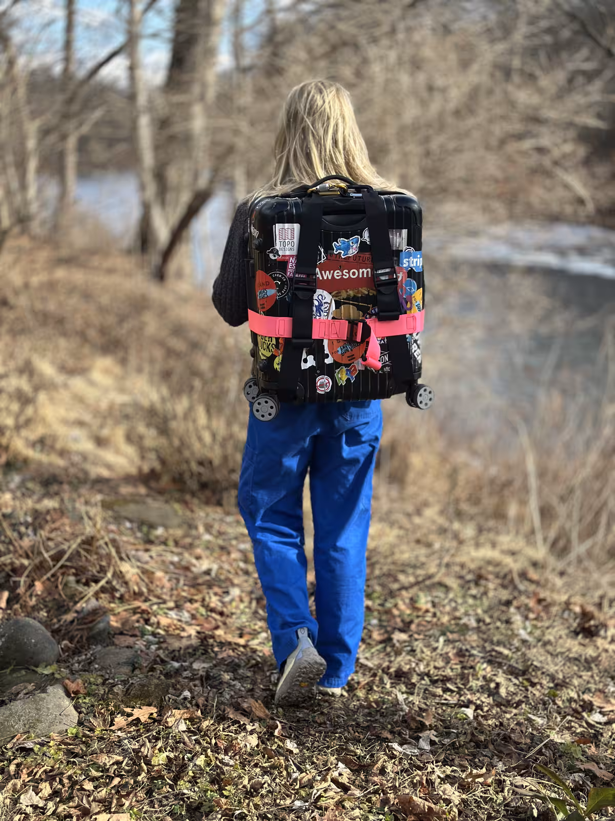 Walking away along a leaf-covered path by a river with the strapped case riding high on the back like a backpack
