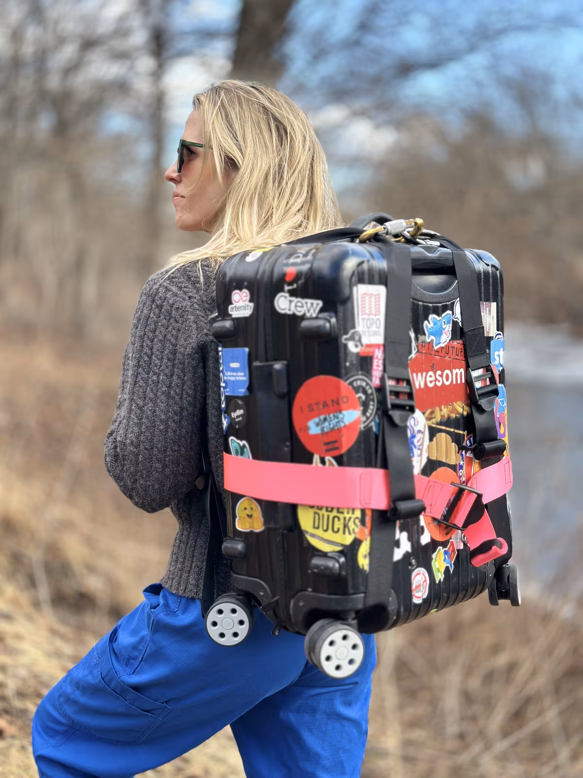 The Rimowa cabin case worn on someone's back as a backpack, held by two black shoulder straps with a pink strap running horizontally around the case